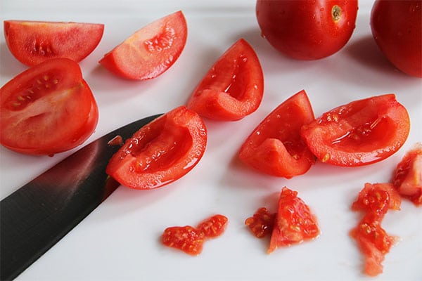 deseeded tomatoes on a white cutting board with a knife.