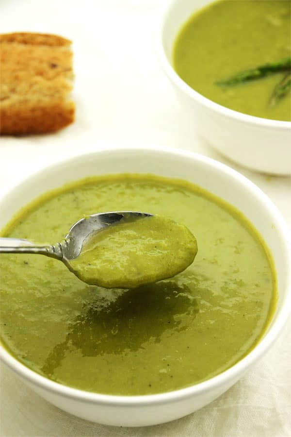 creamy asparagus soup in white bowl with spoon being dipped.