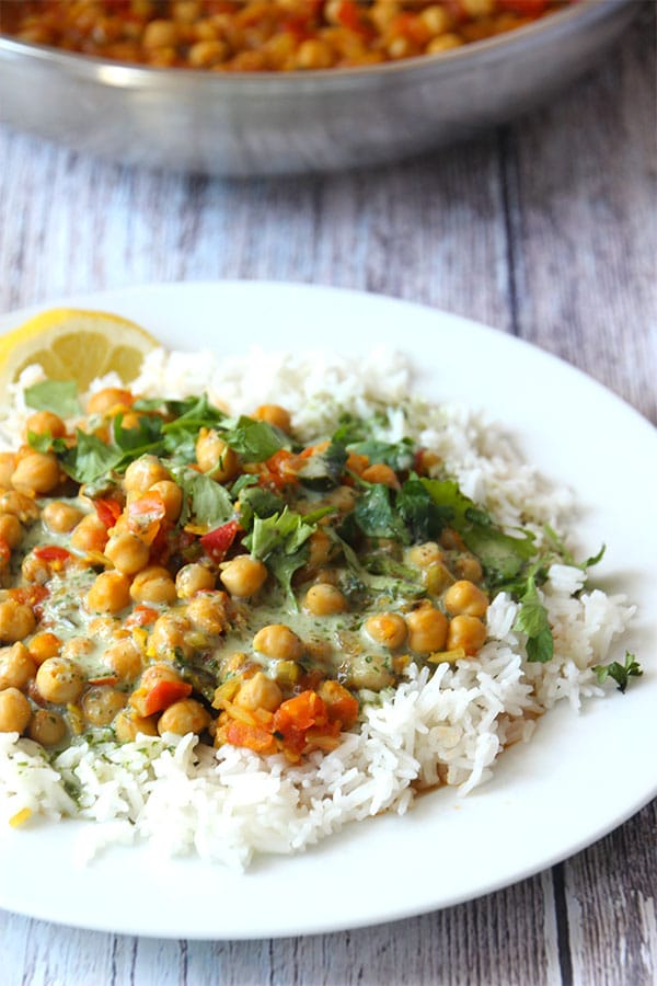 chana masala over white rice on white plate topped with coriander coconut cream and fresh coriander.