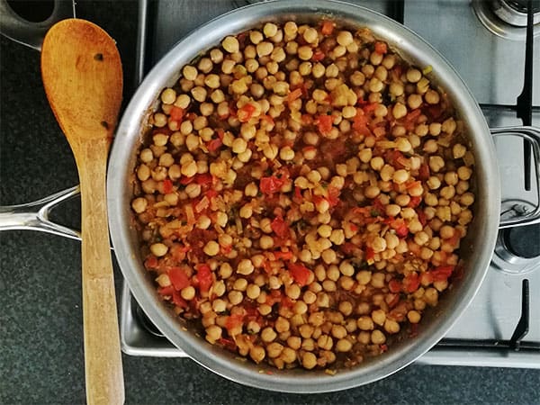 chana masala with tomatoes and chickpeas in stainless steel pan on stove top with wooden spoon.