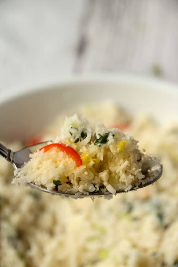 Lemon cauliflower rice is lifted with a spoon over a white bowl.