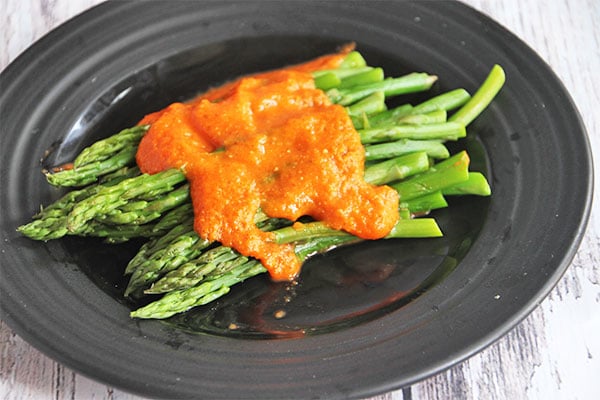 Steamed asparagus on black plate with warm red pepper Romesco sauce over it.