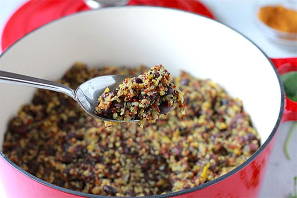 red pot of quinoa & black beans with orange zest and a spoonful being lifted above the pot.