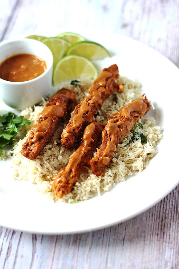 soy strips with satay sauce over cumin-lime cauliflower rice and small dish of satay sauce on white plate.