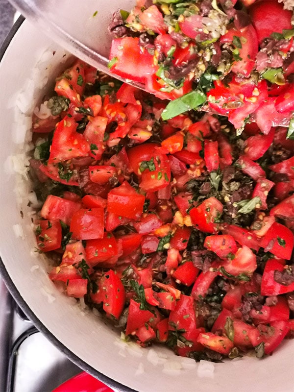 Fresh chopped tomatoes, basil, parsley, oregano, Kalamata olives, capers and lemon juice added to red pot with simmered onions, garlic and red chili flakes.
