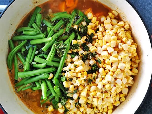 Fresh green beans and corn kernels added to simmering pot.
