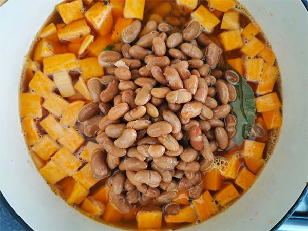 Borlotti (brown beans) added to diced sweet potatoes in pot.