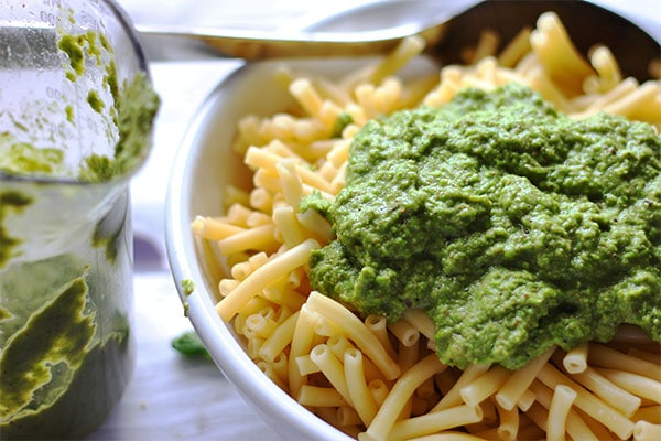 Adding blended pea pesto with peas, vegan Parmesan, fresh basil and garlic to cooked macaroni noodles.
