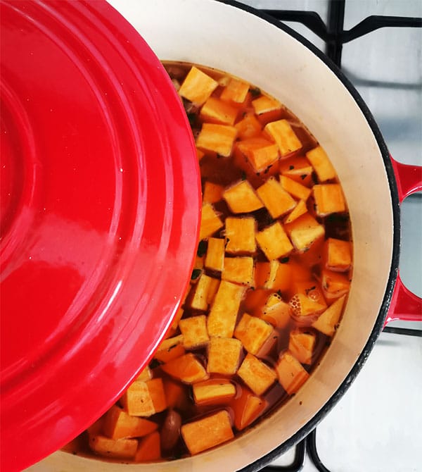 sweet potatoes in red pot being simmered in liquid.