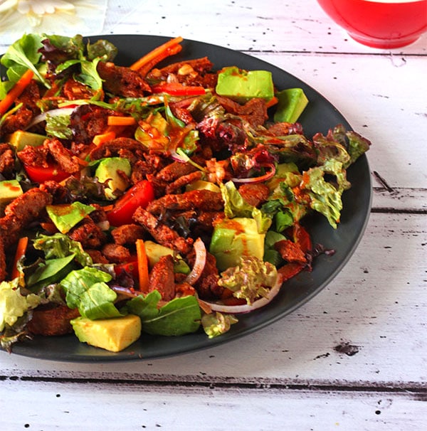 Salad with BBQ soy curls, salad greens, carrots, sliced red onions, red bell peppers, cherry tomatoes and avocado with paprika dressing pour over.