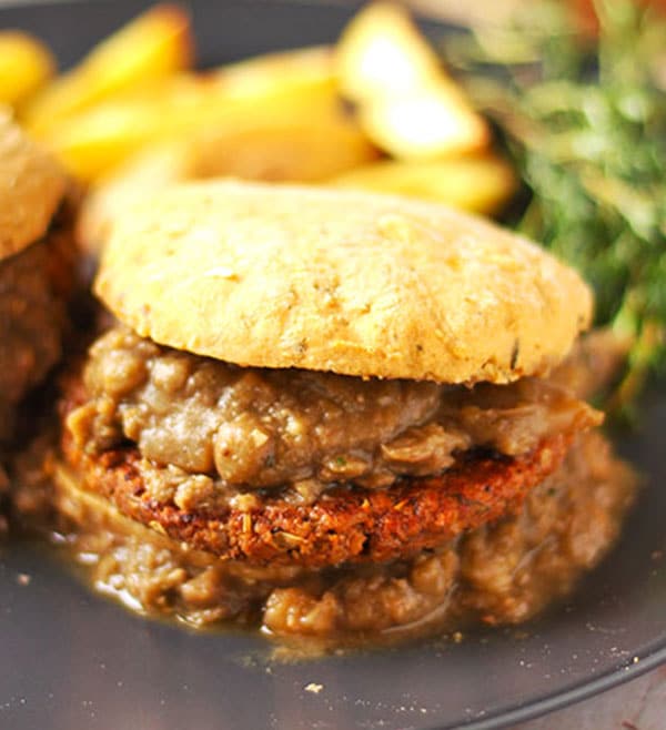 close up shot of sweet potato biscuit loaded with a tempeh sausage patty and smothered in lentil gravy.