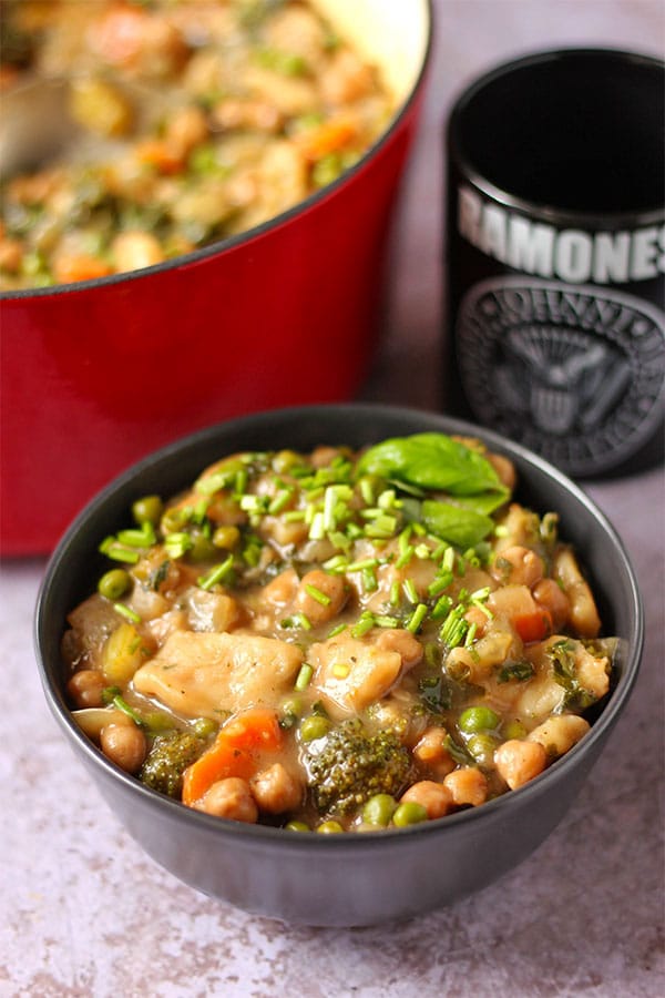 chickpea and vegetable dumpling stew with broccoli, carrots, chickpeas, peas, kale, and fresh basil in gravy all in black bowl.