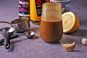 Creamy tahini dressing in jar with ingredients and measuring spoons beside it.