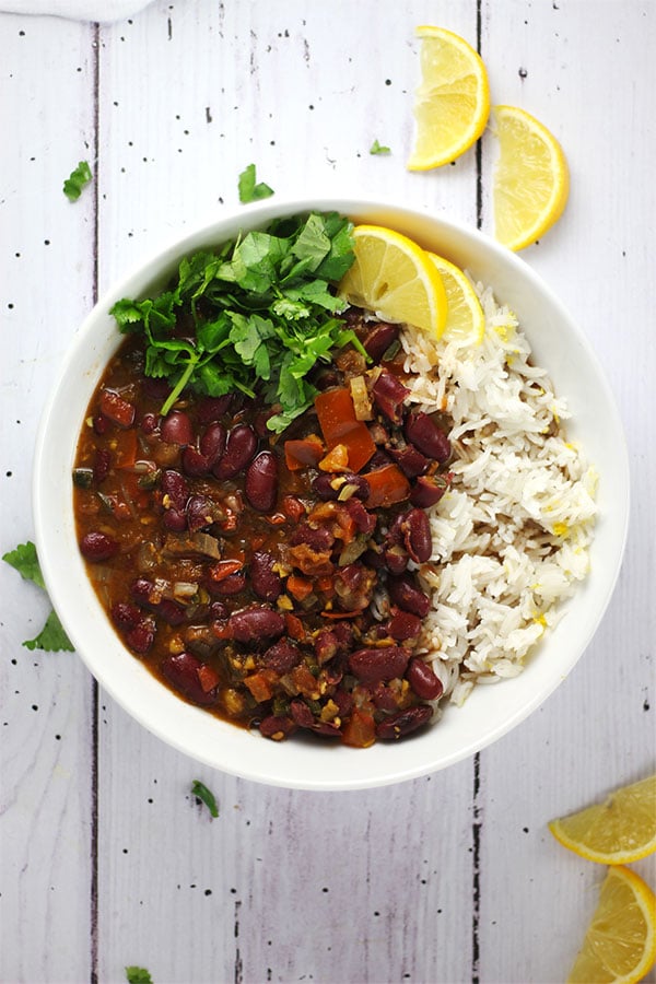 overhead shot of kidney bean curry in white bowl with rice, cilantro and lemon wedges.