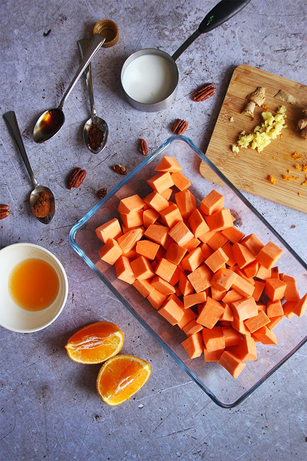 Ingredients for maple pecan sweet potatoes with orange wedges and juice, diced sweet potatoes in glass baking dish.