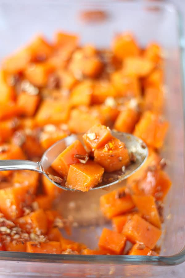 Spoonful of maple pecan sweet potatoes held over clear glass baking dish.