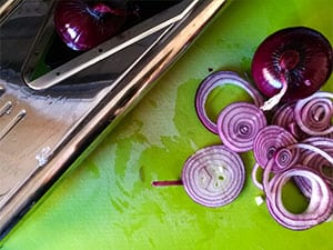 Red onions are sliced using a mandolin.