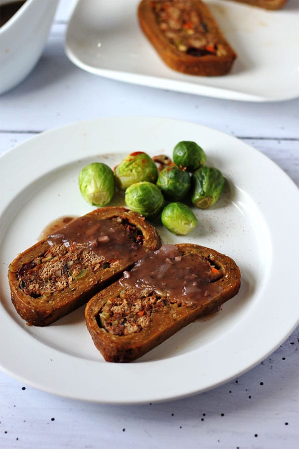 2 slices of stuffed seitan roast with gravy and Brussel's sprouts on white plate.