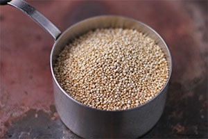Stainless steel measuring cup with dry quinoa in it.