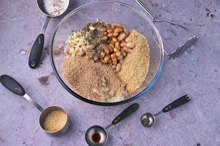 Ingredients for bean balls in glass bowl with spoon of tamari, one of thyme and a cup with nutritional yeast.