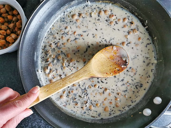 Plant milk is added to chickpeas and rosemary in black skillet.