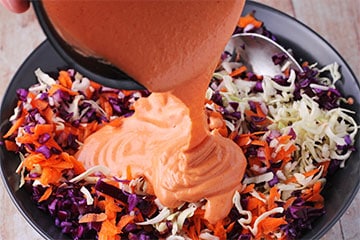 Sriracha dressing poured over cabbage and carrot for spicy coleslaw.
