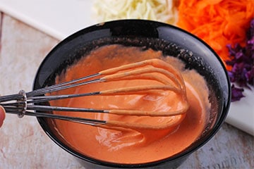 Sriracha dressing in small black bowl with whisk.