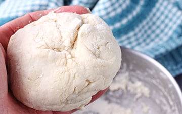 Ball of pasta dough is held in hand.