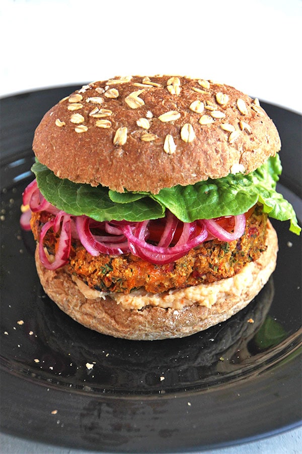 Mediterranean veggie burger recipe makes the perfect burger on a black plate with bun, lettuce and pickled red onions.