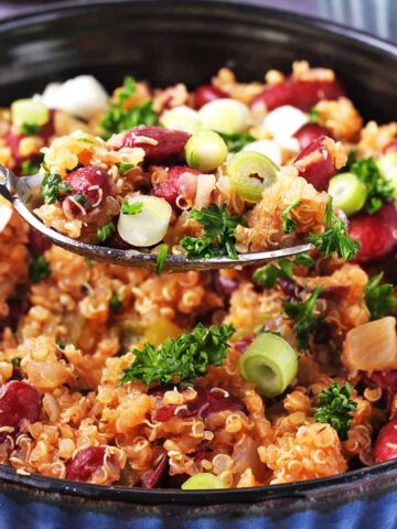 blue bowl of cooked red kidney beans and quinoa with sliced scallions and chopped parsley and spoonful raised above bowl