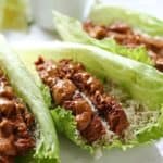 Soy strips with satay sauce on lettuce leaves with cumin-lime cauliflower rice on white plate.