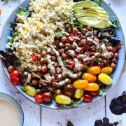 Middle Eastern chickpea salad with lettuce greens, chickpeas, bulgur, cherry tomatoes, dressing and sliced avocado with dish of dressing and dish of spices.