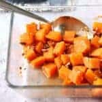 Clear square baking dish with maple pecan sweet potatoes with spoon.