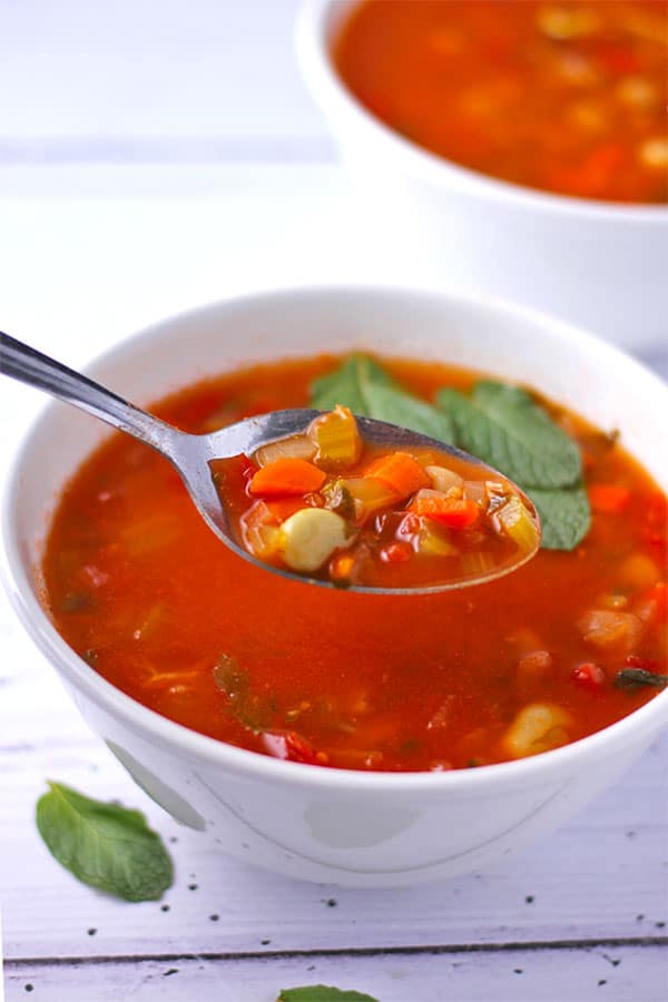 Fava bean soup (broad bean soup or Ful Nabed) with vegetables and tomatoes in white bowl with spoon.