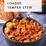 loaded tempeh stew with tempeh, lentils, potatoes, carrots, kidney beans, fava beans, tomato sauce in black bowl with text overlay with recipe title.