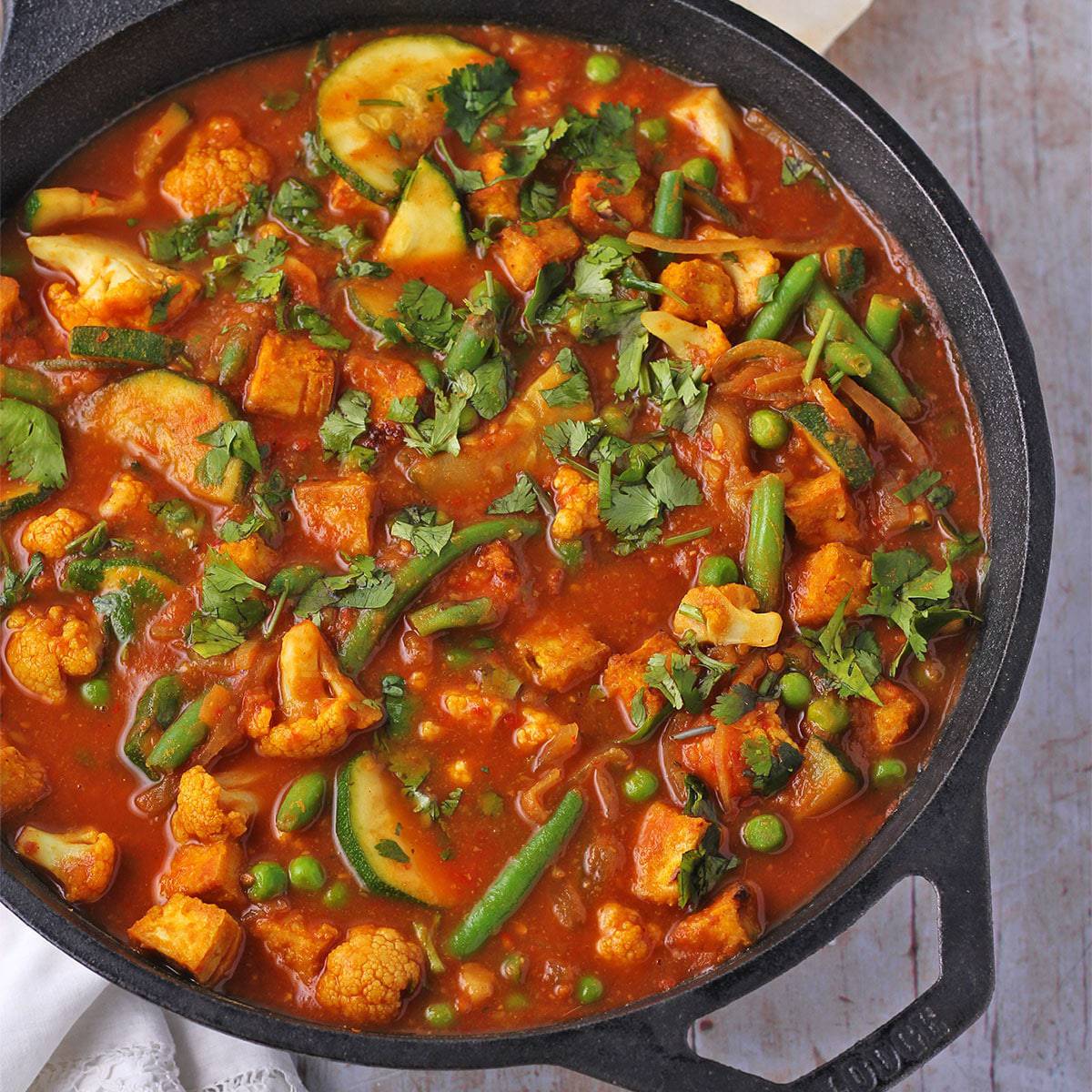 Tomato vegetable curry with crispy tofu in black pan overhead shot.