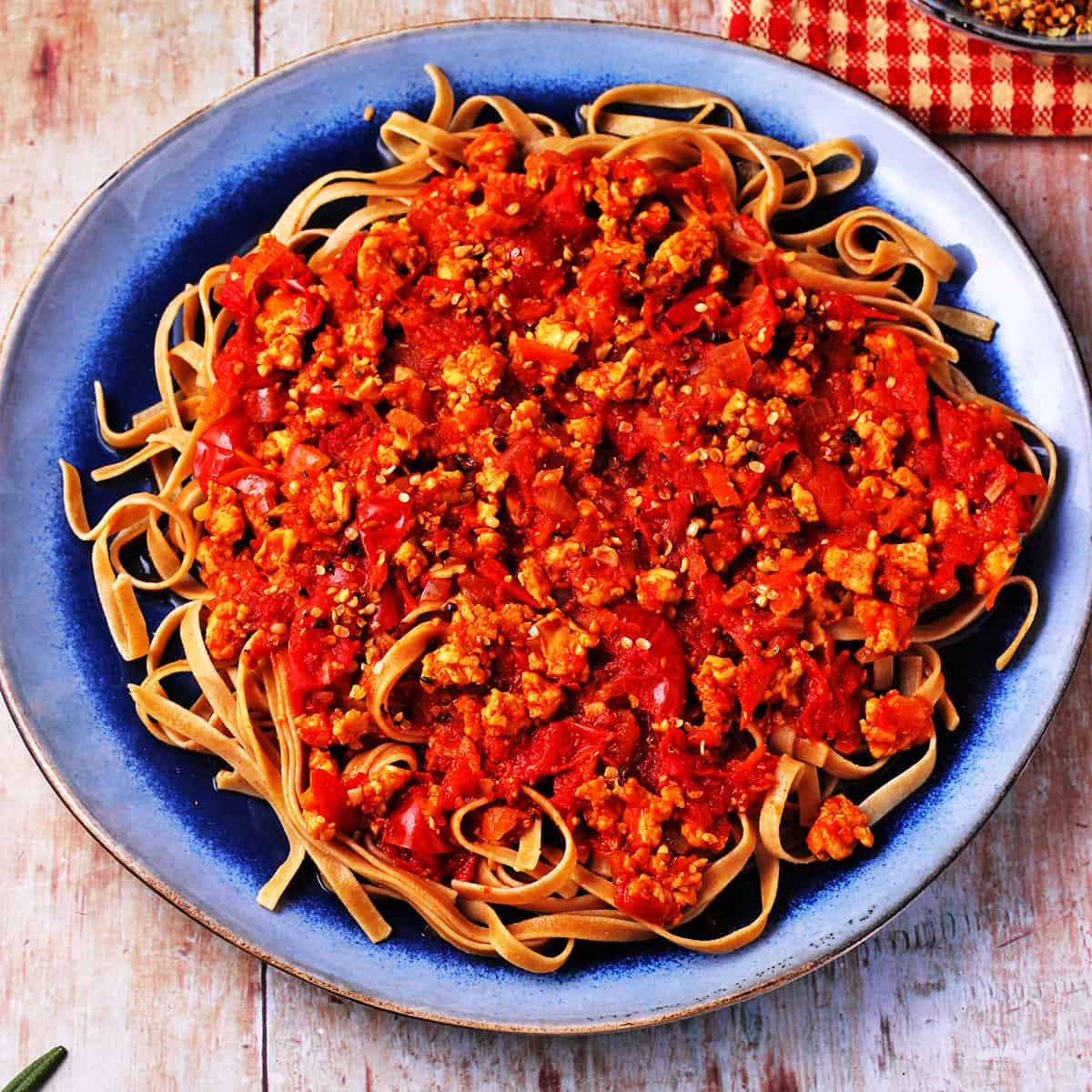 Tempeh Bolognese with wheat tagliatelli pasta on blue plate.