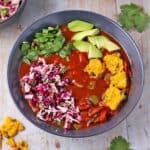 Overhead shot of bowl of black bean chili with cocoa powder topped with jalapeno polenta squares, cabbage slaw, chopped cilantro and avocado cubes