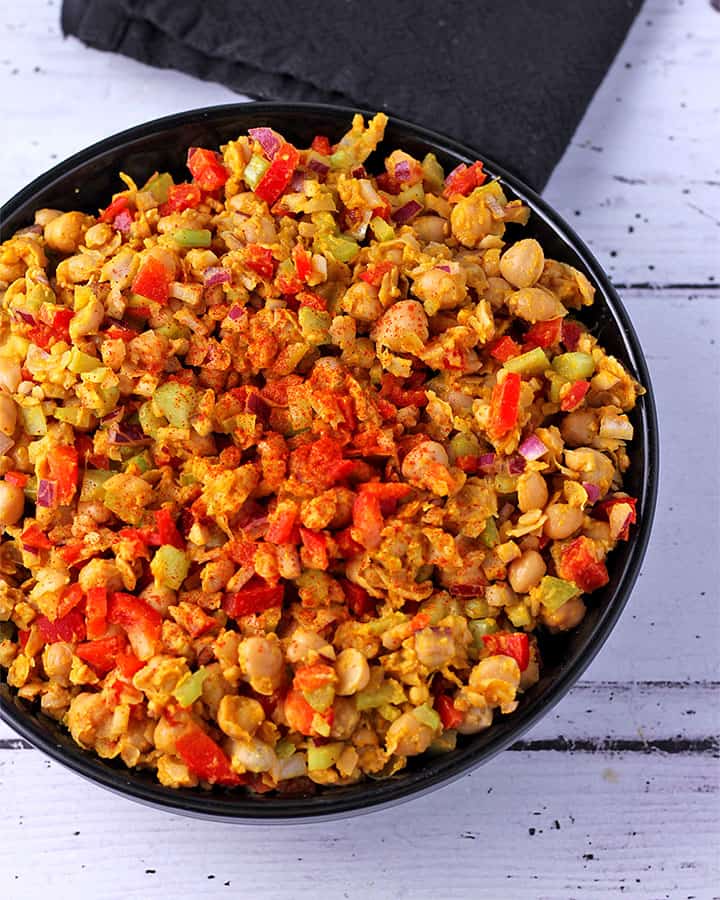 curried chickpea salad with red pepper, celery and onions in black bowl.