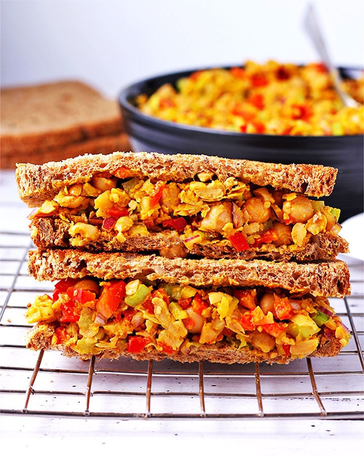 Sandwich made with curried chickpea salad with red pepper, celery and onions on wire rack.