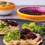 white bean tostadas with blackberry salsa with toasted pepitas and sesame seeds on black plate.