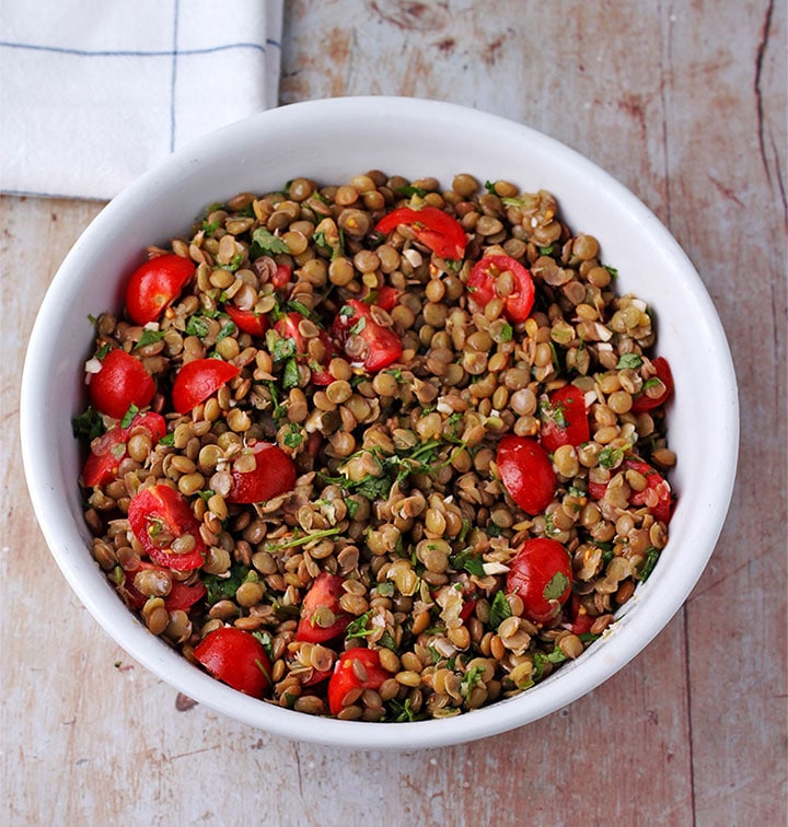 overhead shot of green lentil salad with tomatoes and cilantro in white bowl.