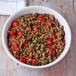 overhead shot of green lentil salad with tomatoes and cilantro in white bowl.