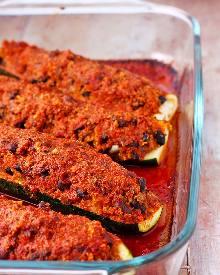 Glass baking dish with baked zucchini boats filled with black beans and quinoa and topped with enchilada sauce