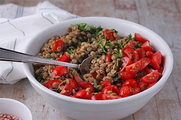 Cooked lentils, sliced cherry tomatoes and chopped cilantro in white bowl mixed with spoon