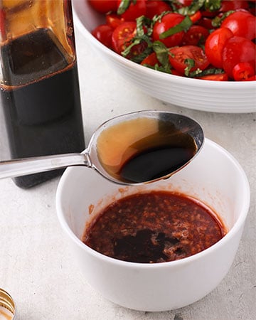 Spoonful of reduced balsamic vinegar is added to dressing in small white bowl.