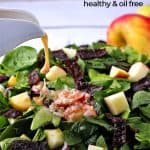 Pouring red wine-Dijon dressing over spinach apple salad with red onion and plant-based bacon