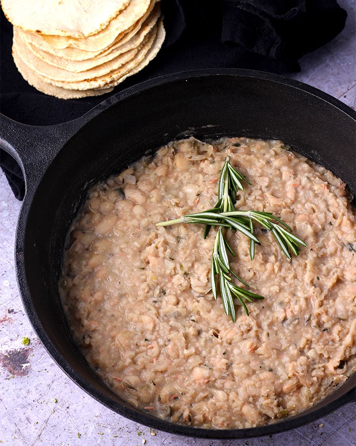 refried white beans with fresh rosemary in black pan