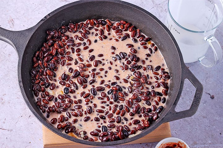 black beans are simmered in black pan with coconut milk, onions, salsa and chipotle peppers