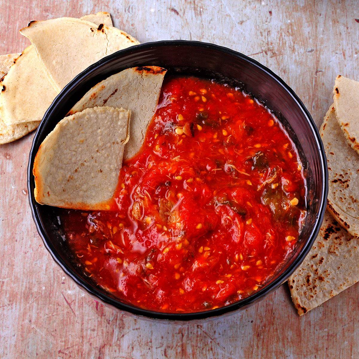 fresh salsa molcajete with roasted tomatoes, jalapenos and garlic in blue bowl with tortilla chips
